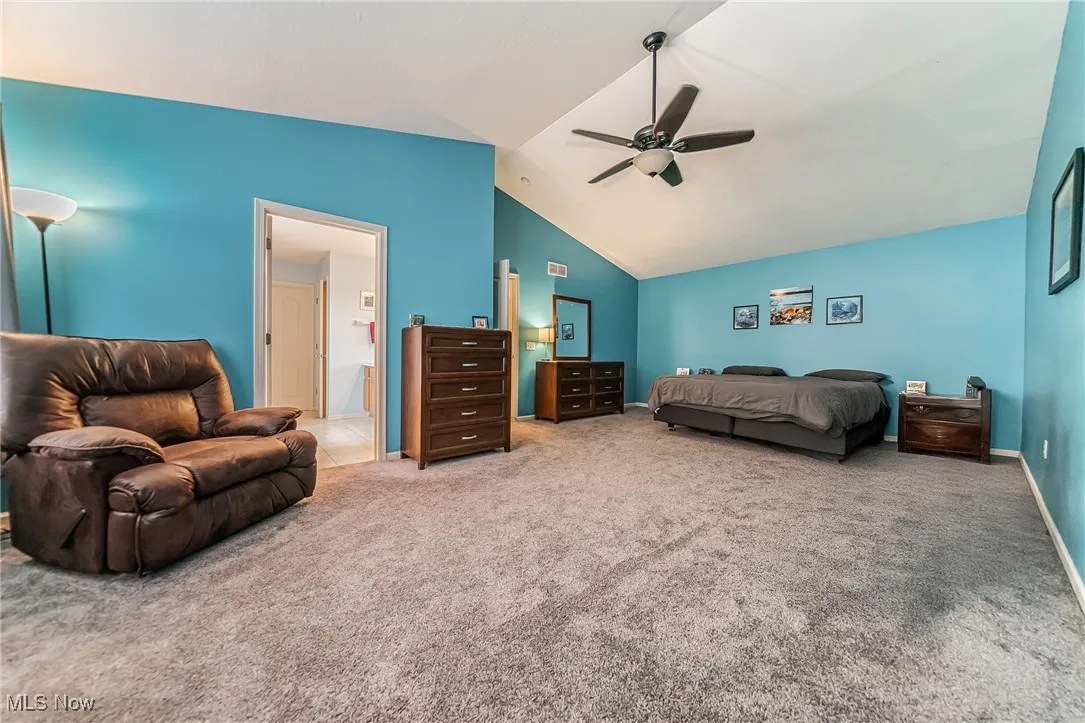 Bedroom featuring vaulted ceiling, carpet, ceiling fan, and ensuite bath