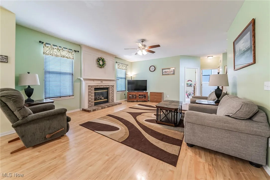 Living room featuring light wood finished floors, a brick fireplace, and ceiling fan