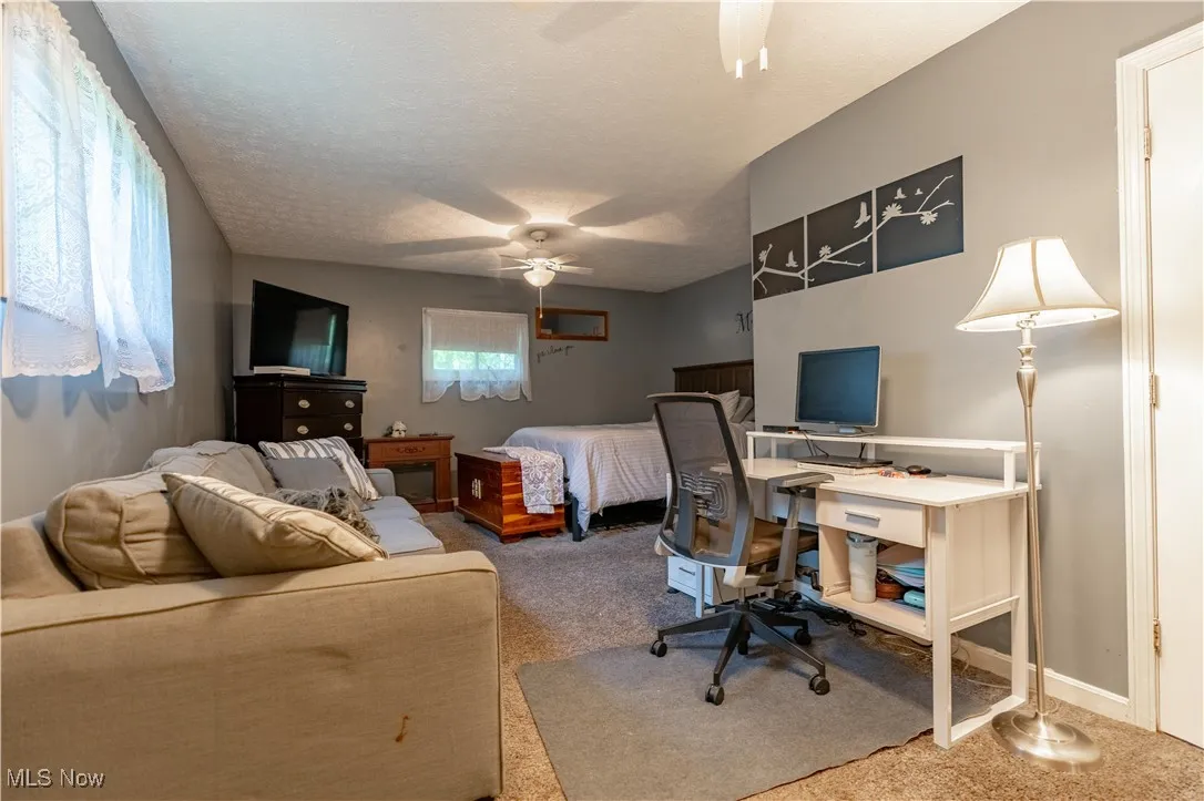 Carpeted bedroom featuring a desk, ceiling fan, and a textured ceiling