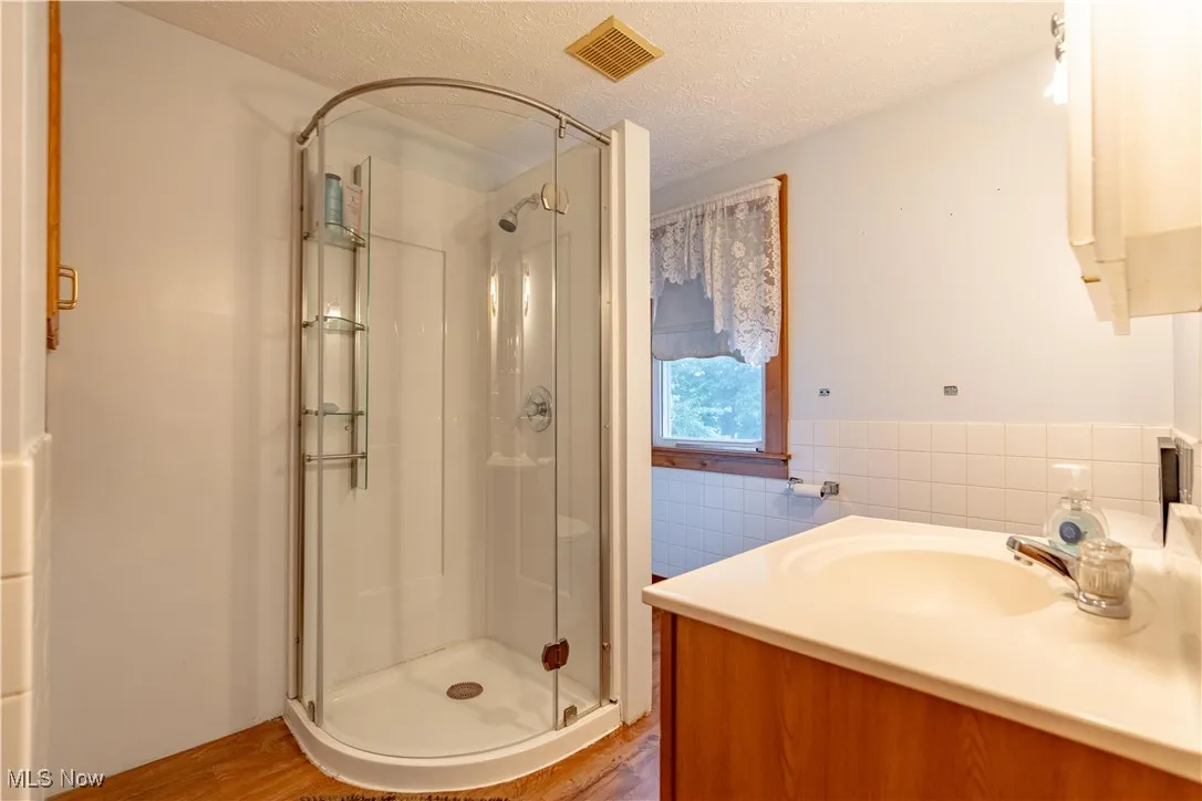 Bathroom with a shower stall, a textured ceiling, tile walls, wood finished floors, and a wainscoted wall