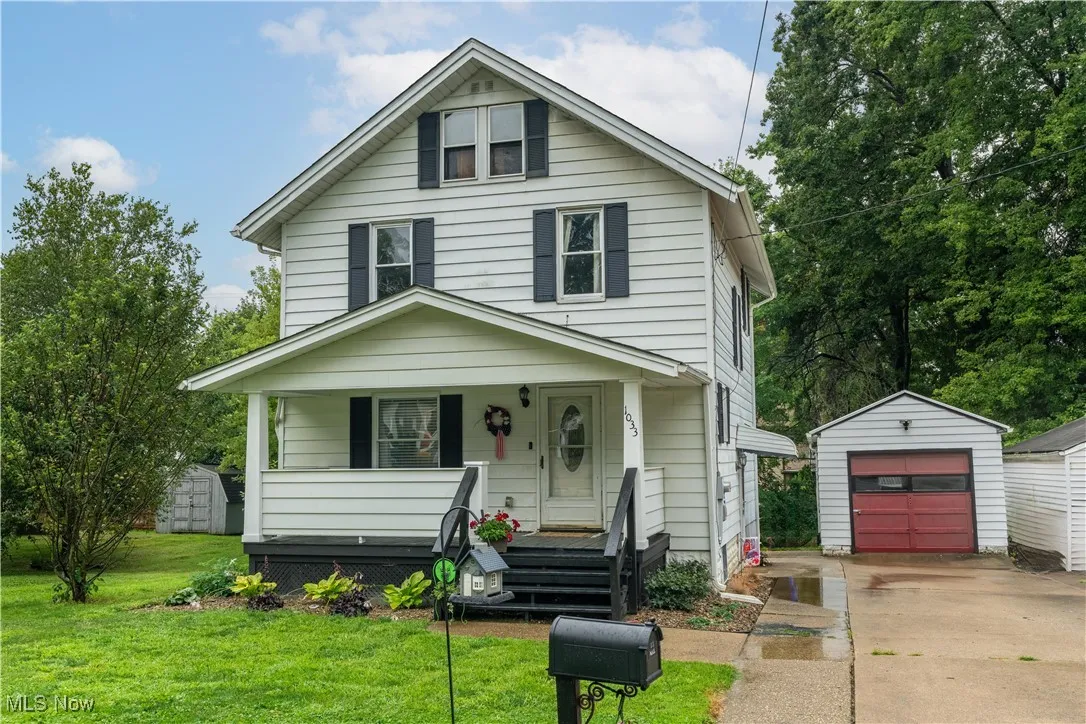 American foursquare style home featuring an outbuilding, covered porch, concrete driveway, and a front yard