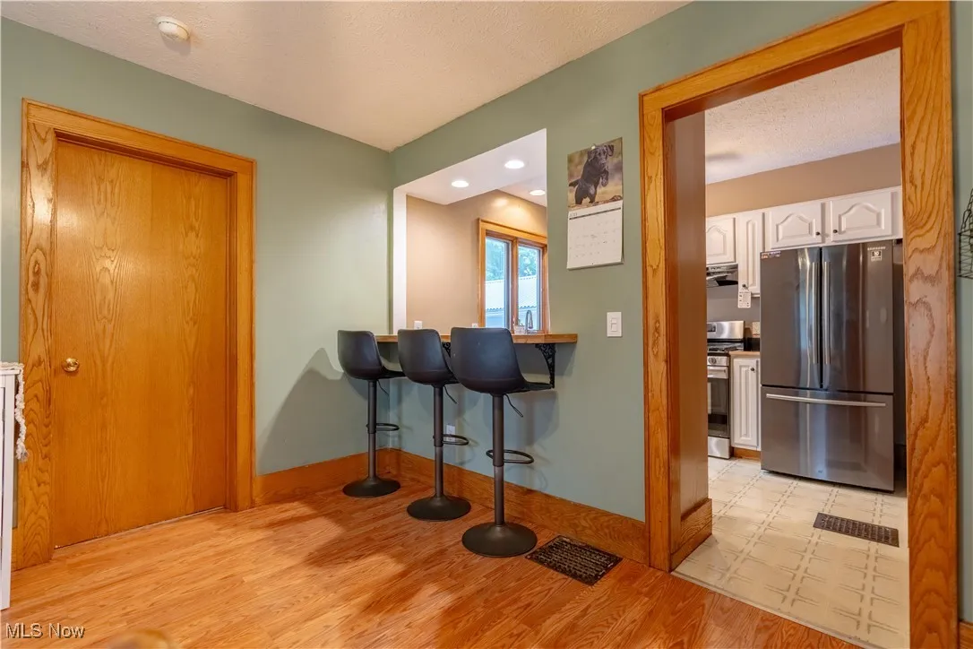Kitchen featuring appliances with stainless steel finishes, light wood-style flooring, white cabinets, a textured ceiling, and a kitchen bar