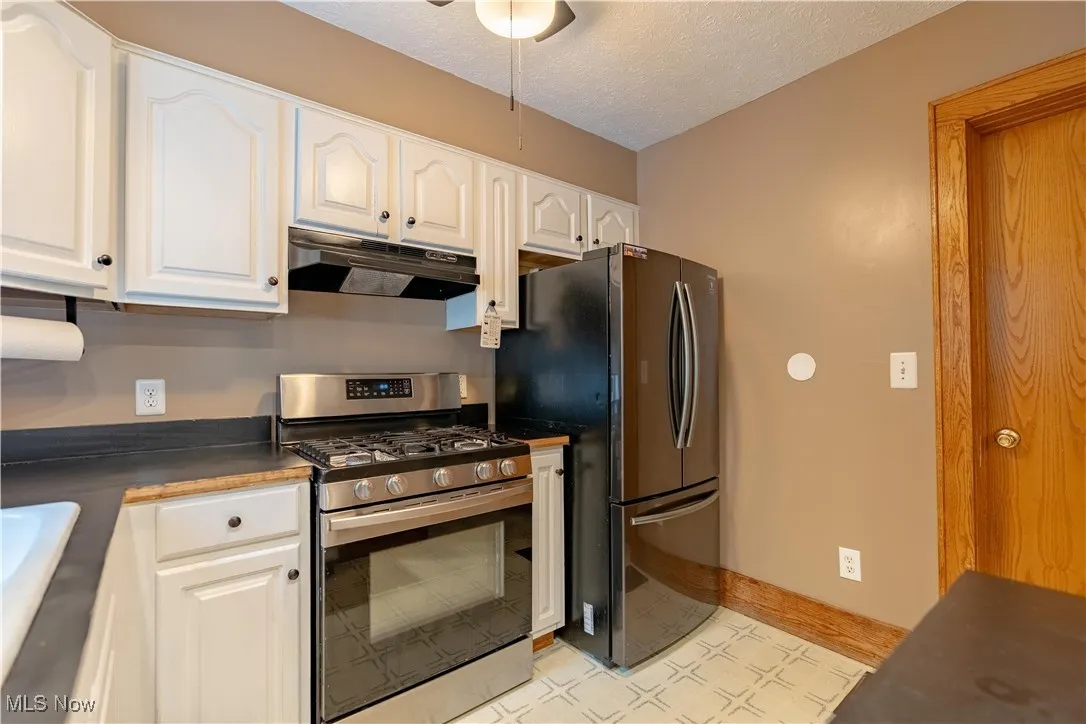 Kitchen featuring stainless steel gas range oven, a textured ceiling, under cabinet range hood, dark countertops, and white cabinets