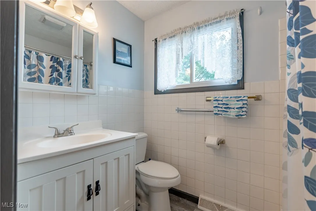 Full bathroom featuring vanity, tile walls, wainscoting, and a shower with curtain