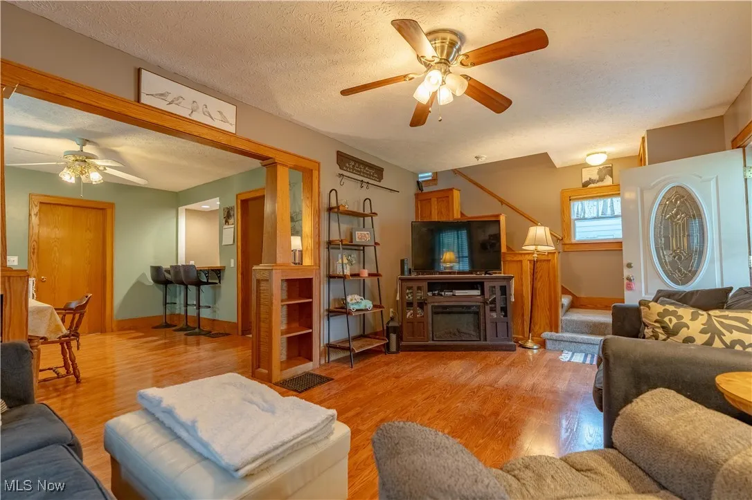 Living area with ceiling fan, light wood-style floors, a textured ceiling, and a fireplace