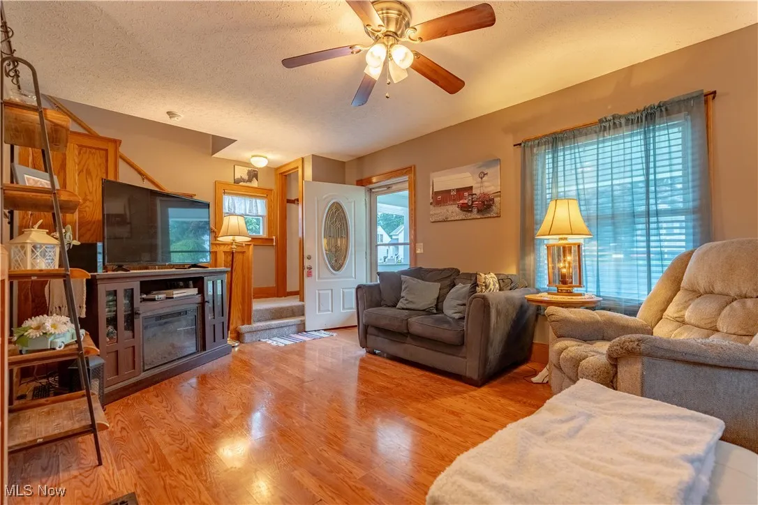 Living room with a textured ceiling, light wood-style floors, and ceiling fan