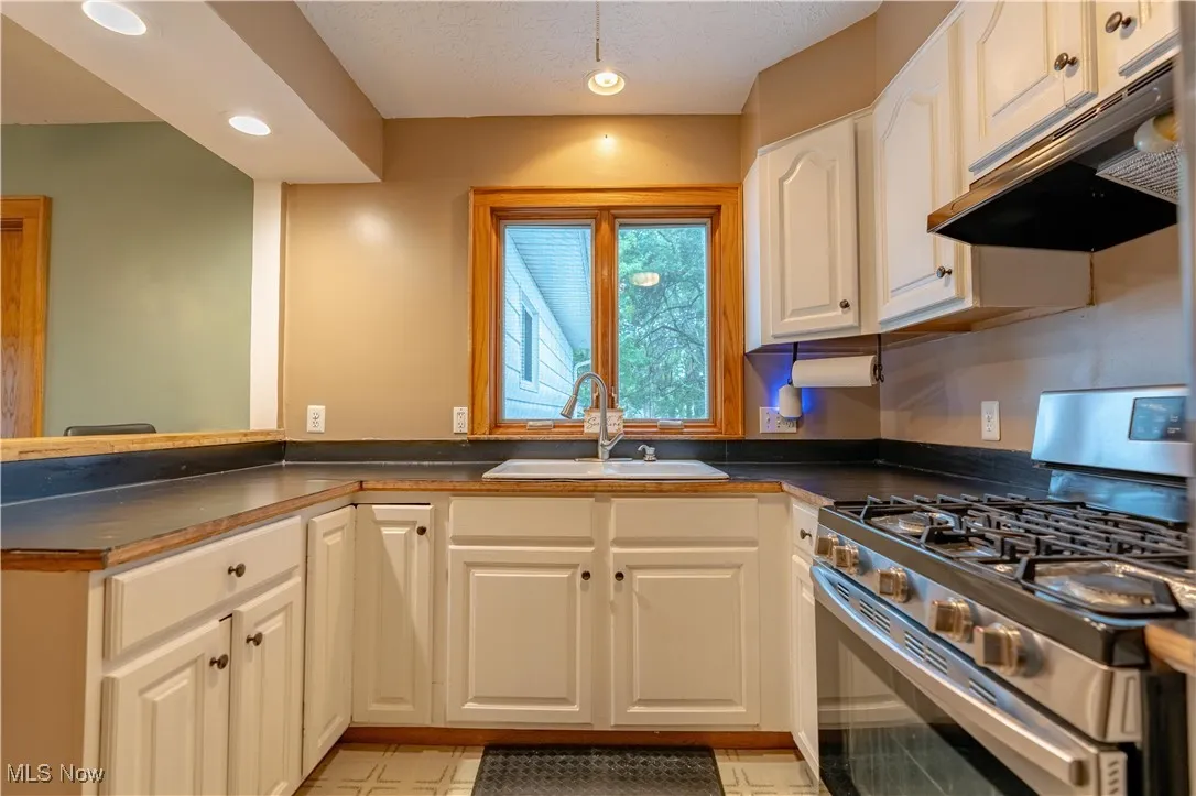Kitchen featuring stainless steel gas range oven, dark countertops, under cabinet range hood, recessed lighting, and a textured ceiling