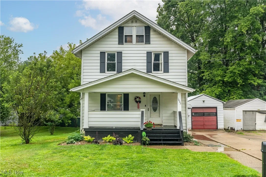 American foursquare style home with a porch, an outdoor structure, a front yard, driveway, and a garage