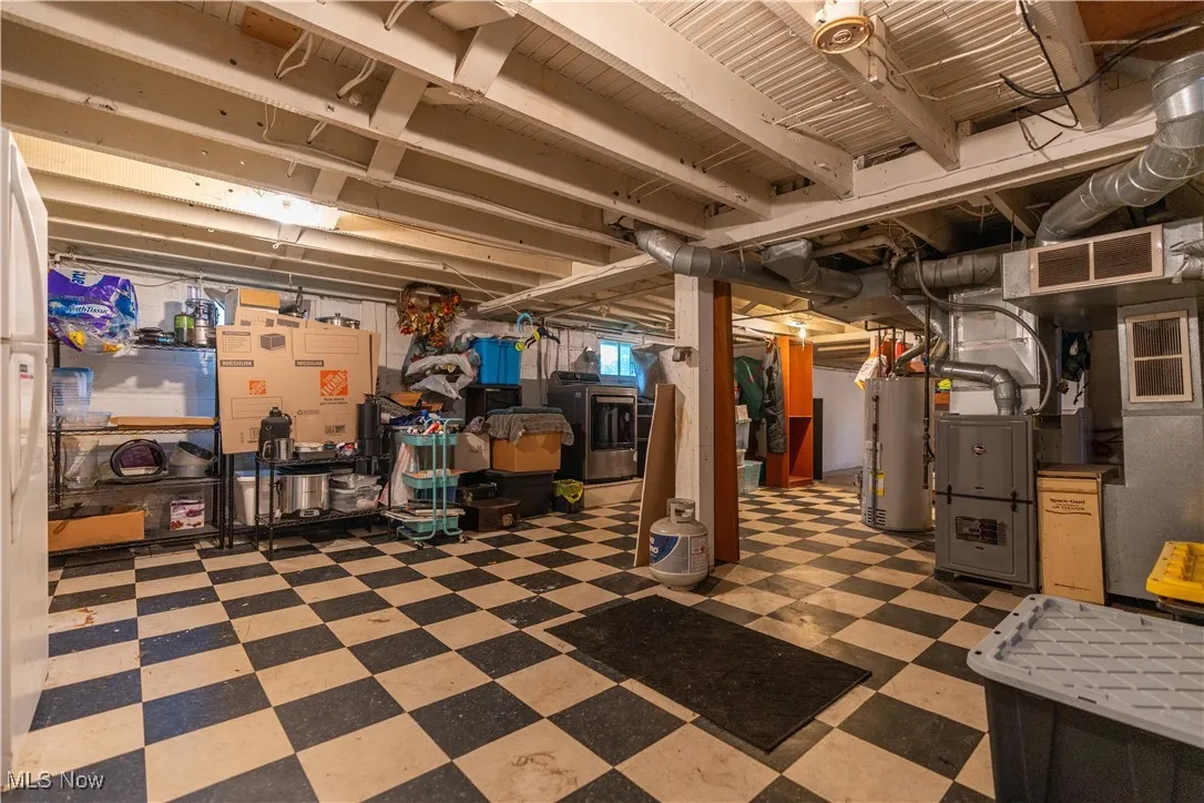 Unfinished basement featuring light flooring, washer / dryer, water heater, freestanding refrigerator, and heating unit