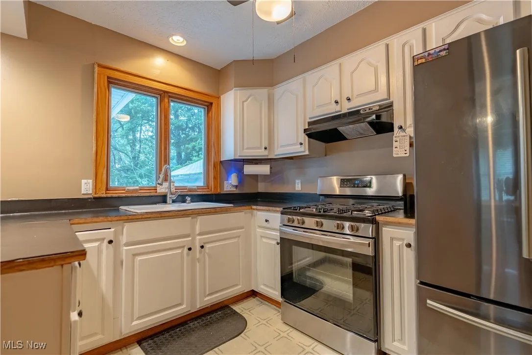 Kitchen featuring appliances with stainless steel finishes, under cabinet range hood, white cabinets, a textured ceiling, and dark countertops