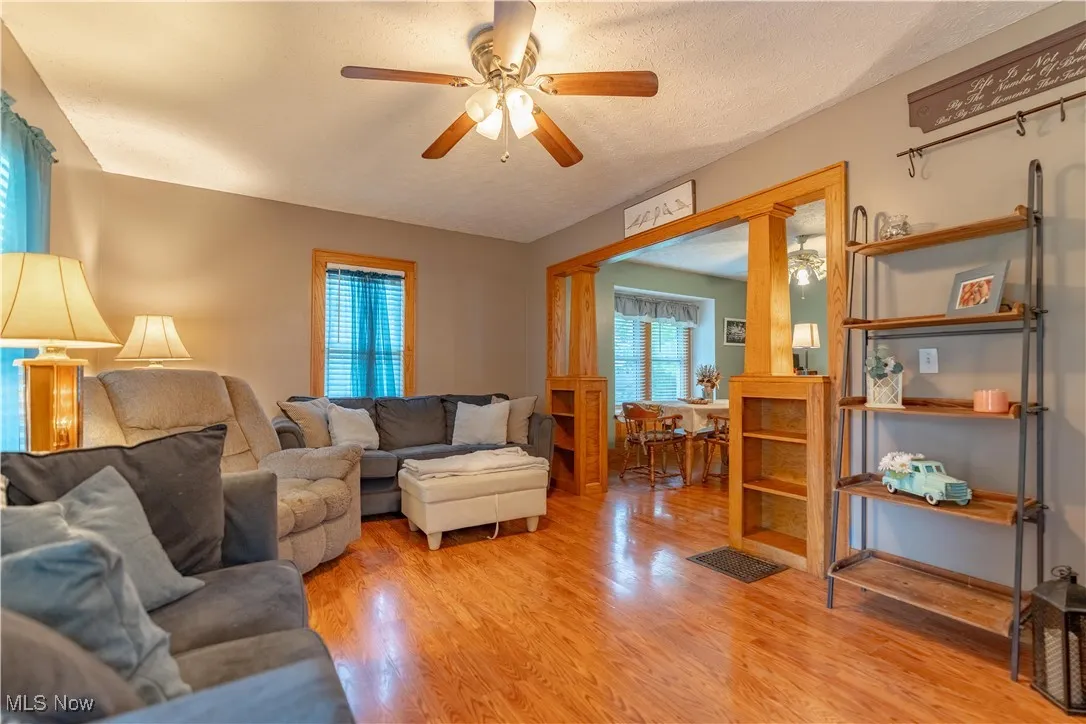 Living area with light wood-style floors, ornate columns, a textured ceiling, and ceiling fan