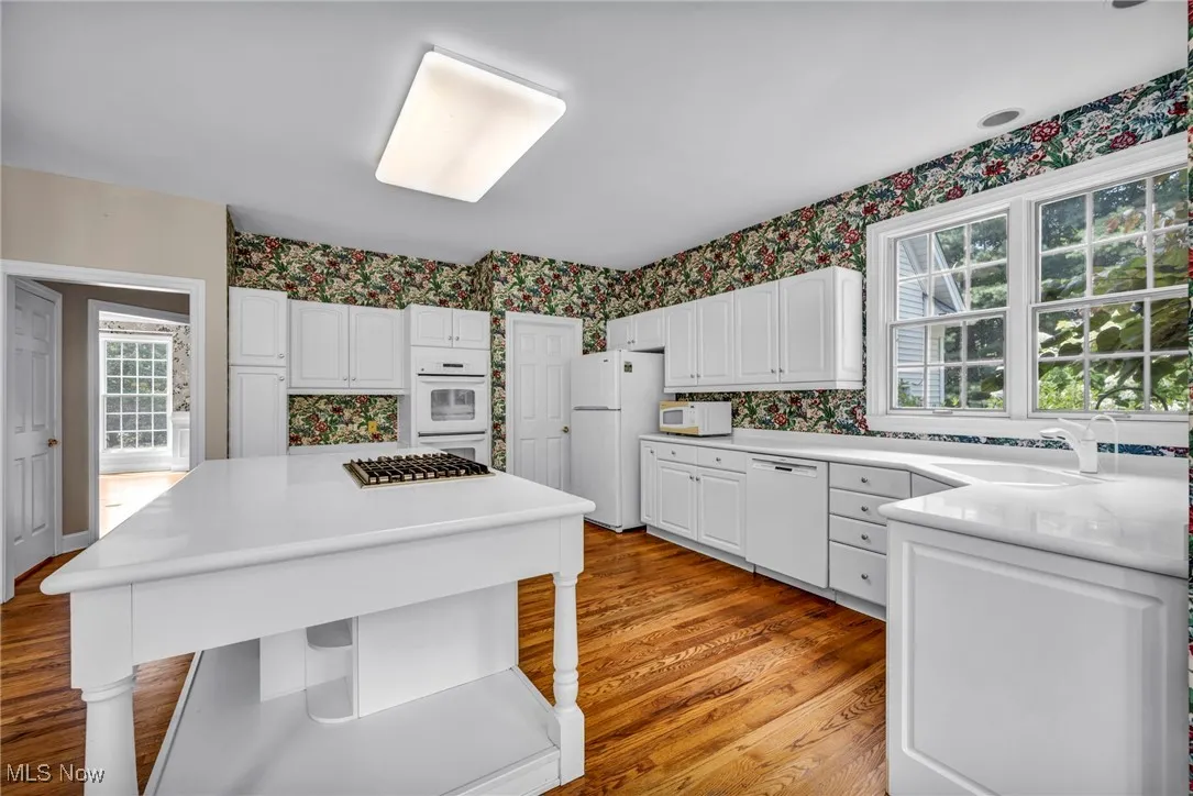 Kitchen featuring wallpapered walls, white cabinetry, light wood-type flooring, white appliances, and light countertops