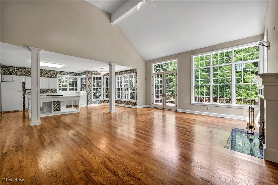 Unfurnished living room featuring ceiling fan, beamed ceiling, light wood-style flooring, a fireplace, and decorative columns