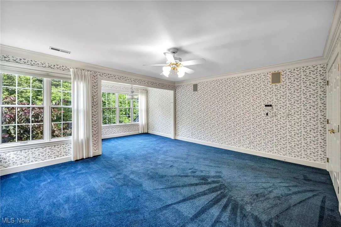 Unfurnished living room with crown molding, carpet flooring, a ceiling fan, and wallpapered walls
