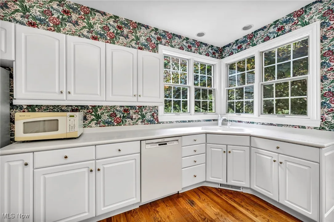 Kitchen featuring wallpapered walls, white appliances, wood finished floors, light countertops, and white cabinetry