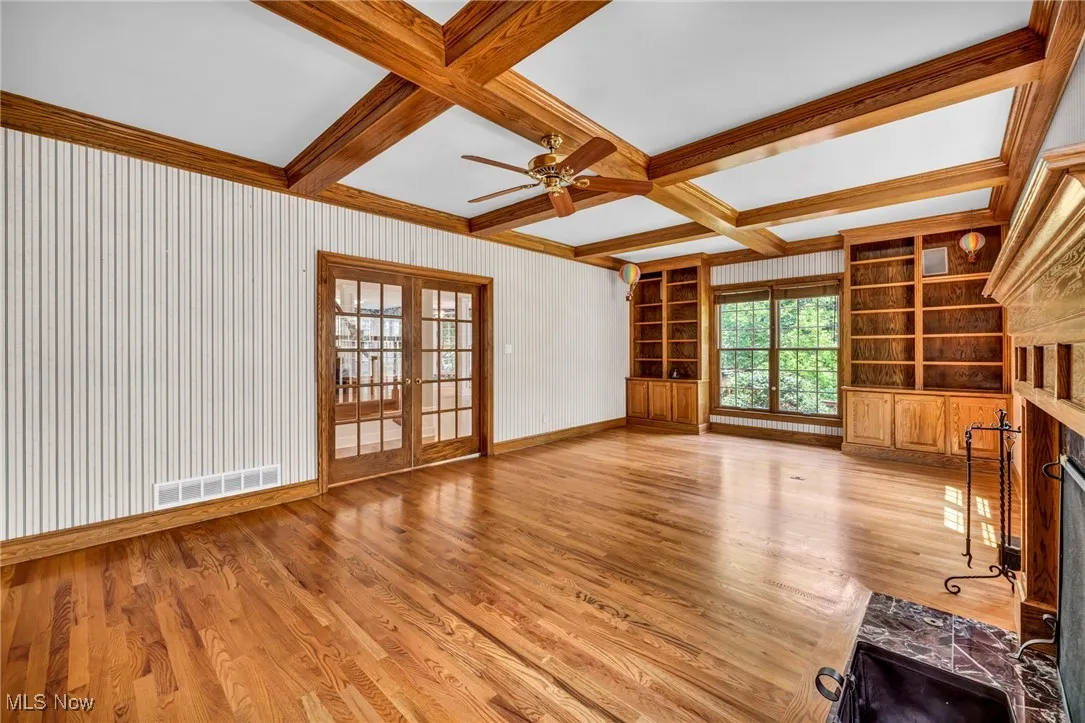 Unfurnished living room featuring coffered ceiling, wood finished floors, beamed ceiling, a fireplace, and built in shelves