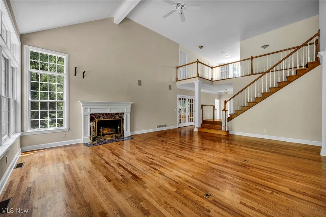 Unfurnished living room featuring light wood-style floors, high vaulted ceiling, beamed ceiling, stairway, and a premium fireplace