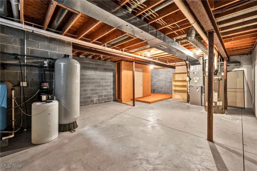 Unfinished below grade area with heating unit, water heater, and a water pressure tank