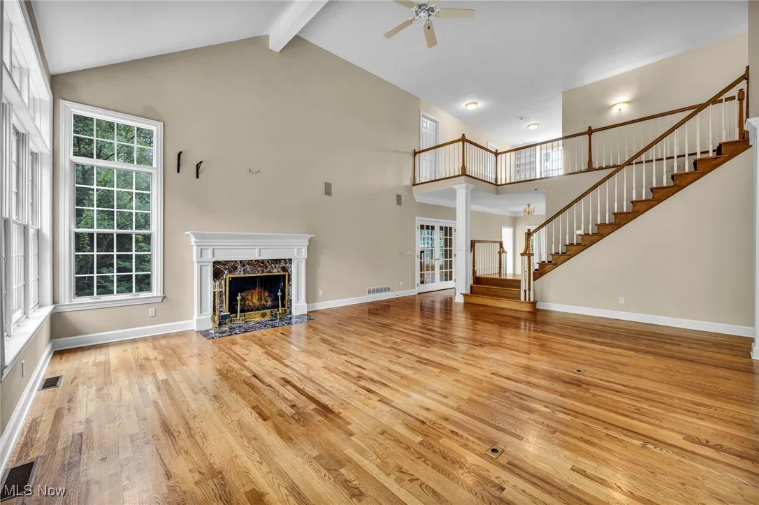 Unfurnished living room featuring stairway, light wood-style floors, a premium fireplace, beamed ceiling, and high vaulted ceiling