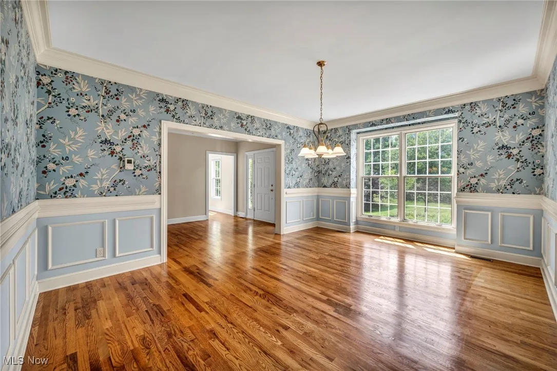 Unfurnished dining area with wallpapered walls, a chandelier, a decorative wall, ornamental molding, and wood finished floors