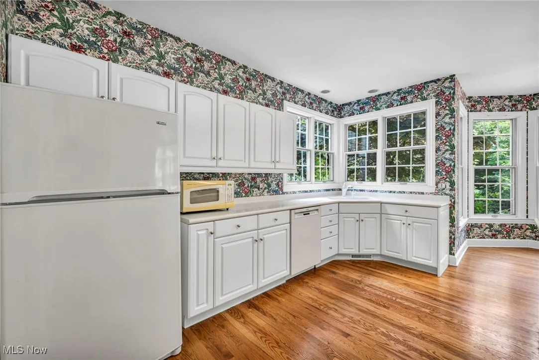 Kitchen featuring wallpapered walls, white appliances, white cabinetry, light countertops, and light wood-style floors
