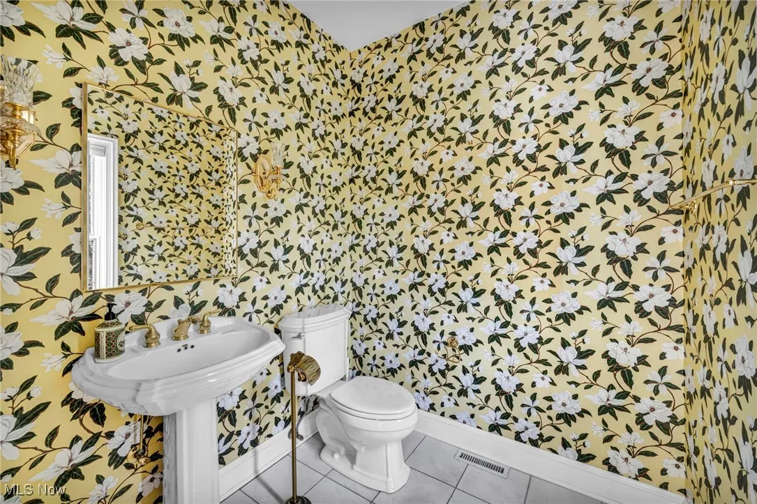 Half bathroom featuring wallpapered walls and tile patterned flooring