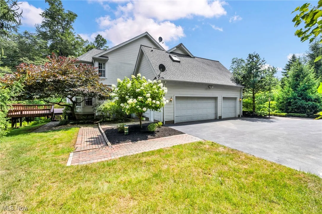 View of side of home with driveway, an attached garage, a shingled roof, and a lawn