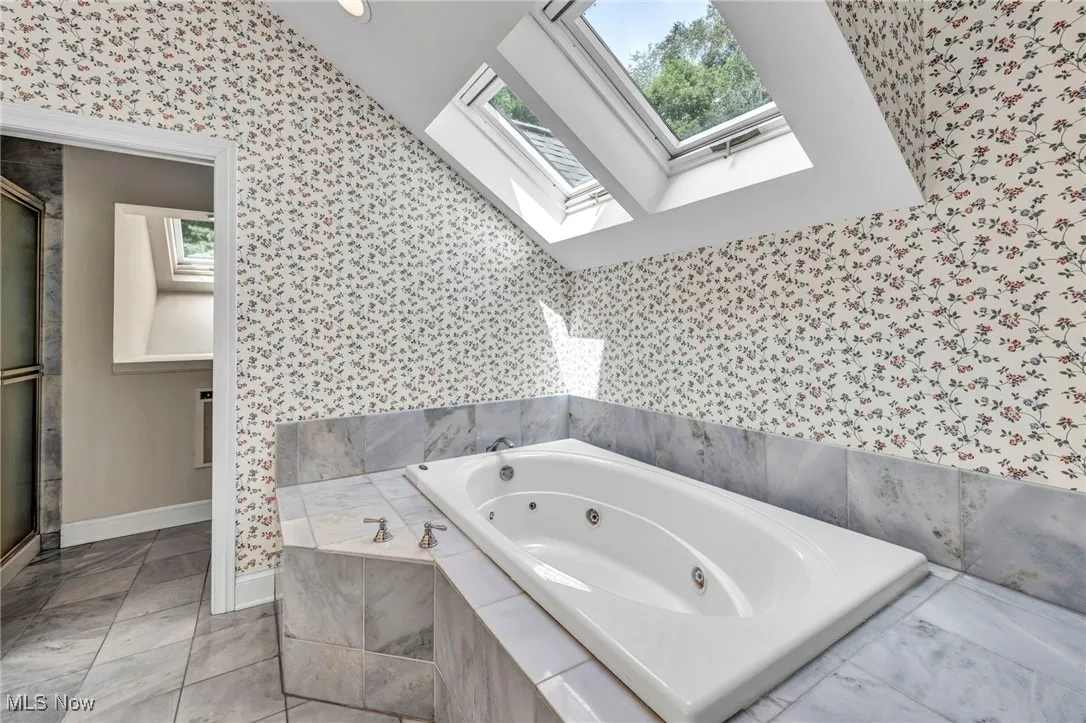 Full bath featuring wallpapered walls, a jetted tub, a skylight, and a shower stall