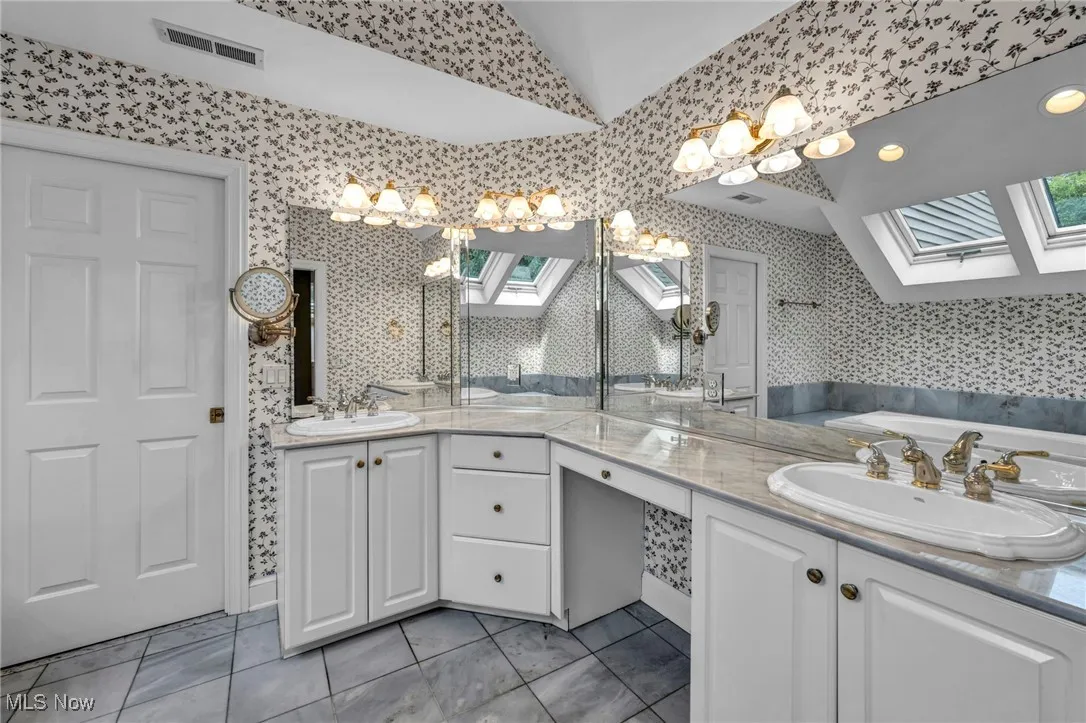 Full bathroom featuring a skylight, plenty of natural light, double vanity, wallpapered walls, and a garden tub