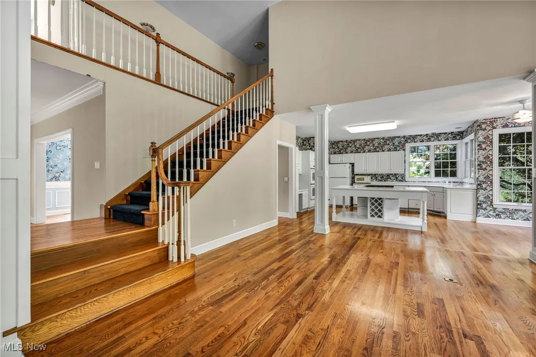 Unfurnished living room featuring light wood finished floors, stairs, a towering ceiling, wallpapered walls, and ornamental molding