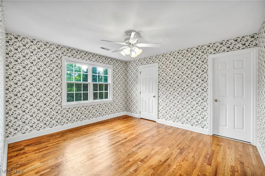 Unfurnished bedroom with light wood finished floors, wallpapered walls, and a ceiling fan