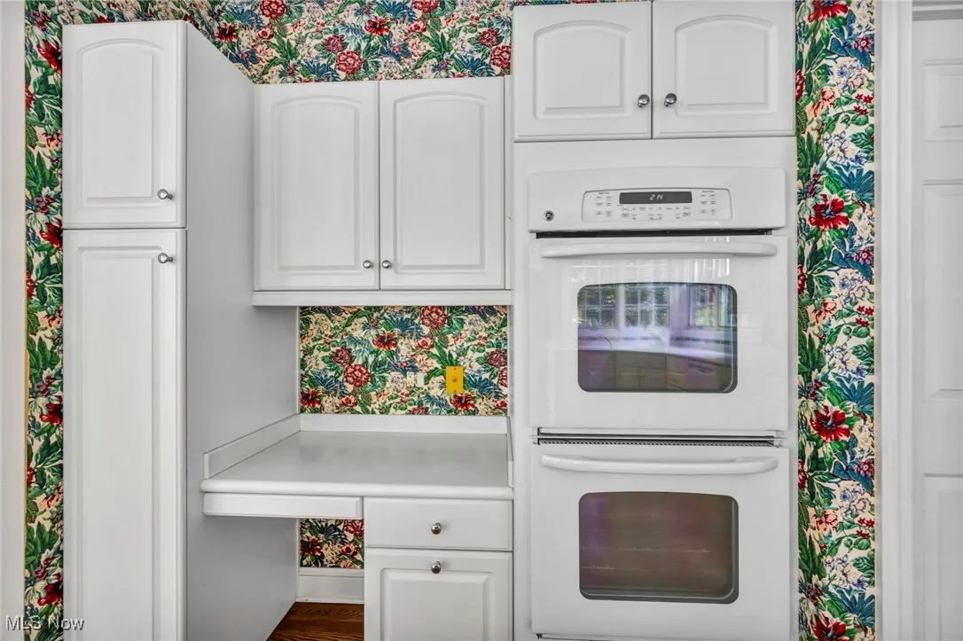 Kitchen featuring white double oven, wallpapered walls, white cabinets, and light countertops