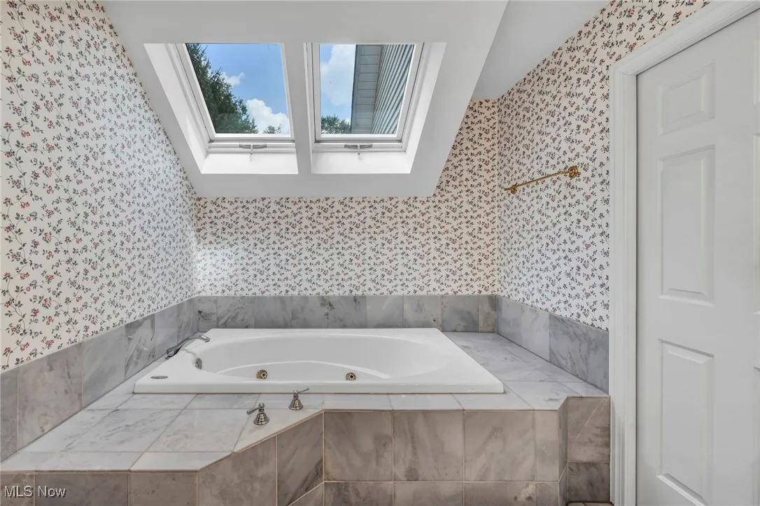 Full bathroom featuring a tub with jets, wallpapered walls, and a skylight