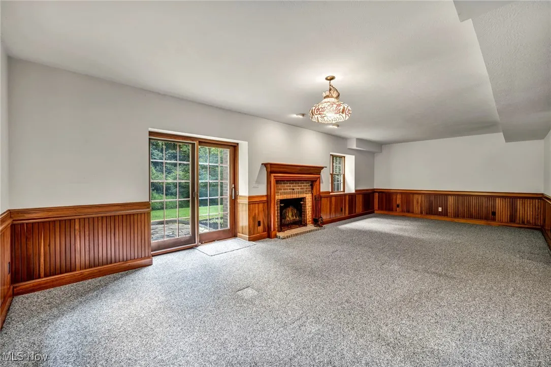 Unfurnished living room featuring a brick fireplace, wainscoting, carpet floors, and wooden walls