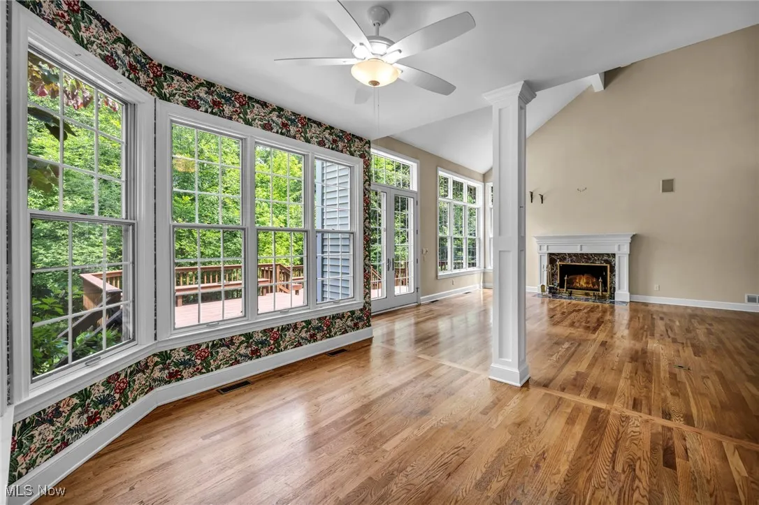 Unfurnished living room featuring vaulted ceiling, a high end fireplace, ceiling fan, wood finished floors, and decorative columns