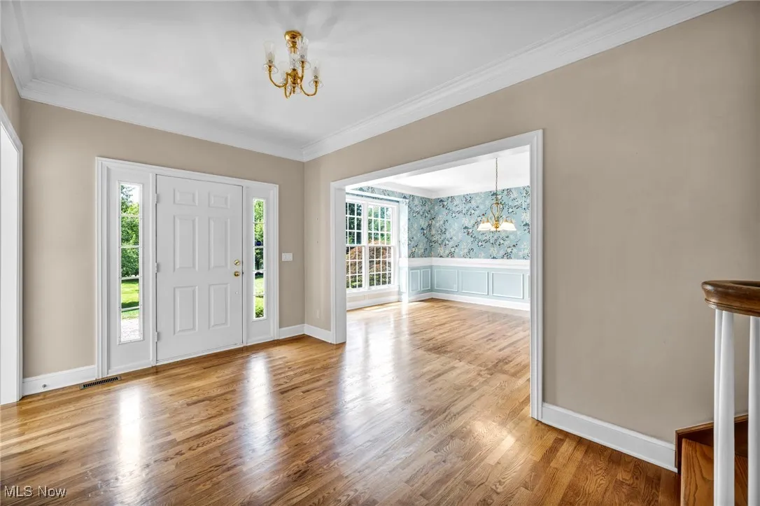 Foyer featuring a chandelier, wainscoting, ornamental molding, wood finished floors, and a decorative wall
