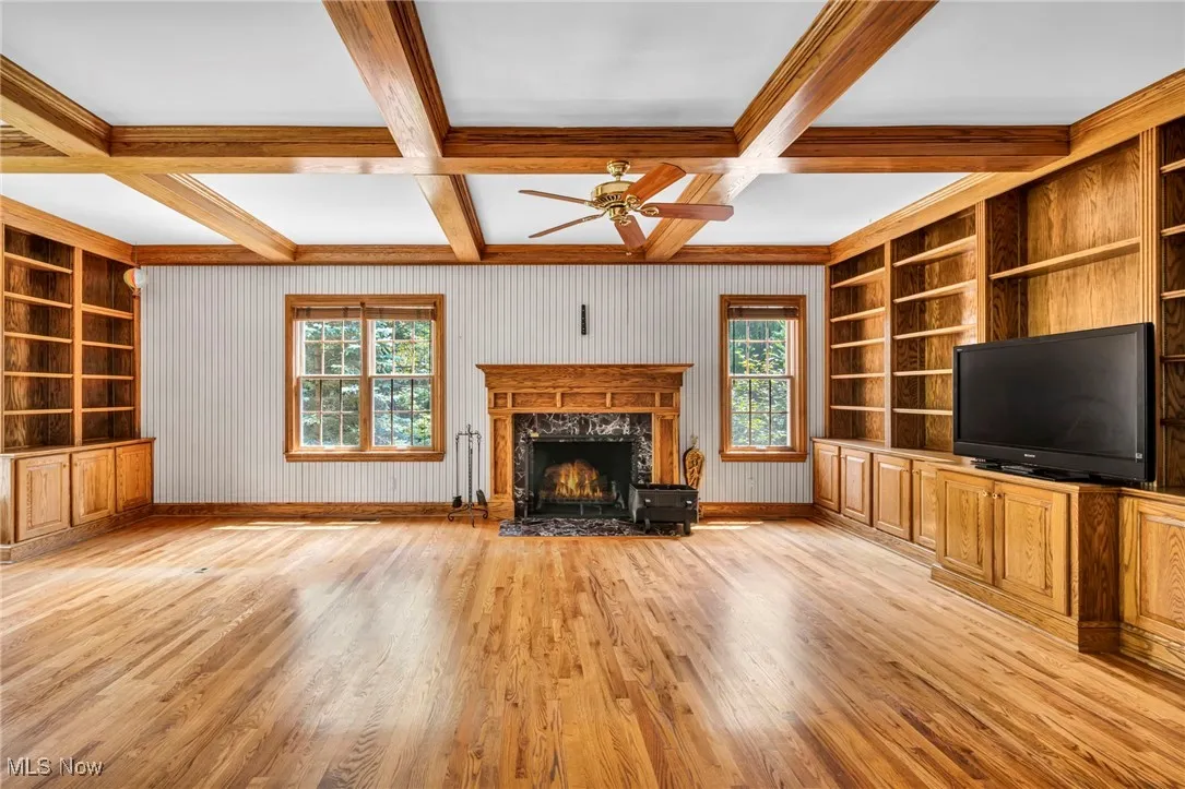Unfurnished living room with built in shelves, beamed ceiling, light wood-type flooring, coffered ceiling, and a high end fireplace