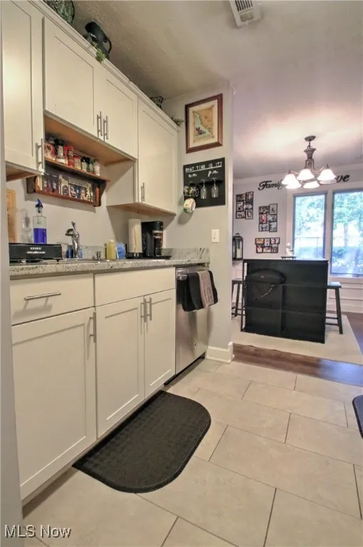 Kitchen with light tile patterned flooring, white cabinets, dishwasher, and a chandelier