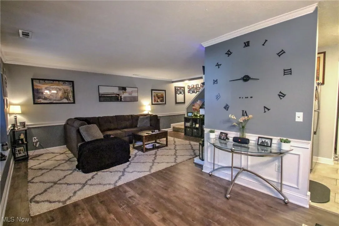 Living room with ornamental molding, wood finished floors, stairway, and wainscoting