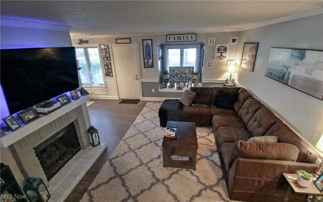 Living room with ornamental molding, wood finished floors, and a fireplace with raised hearth