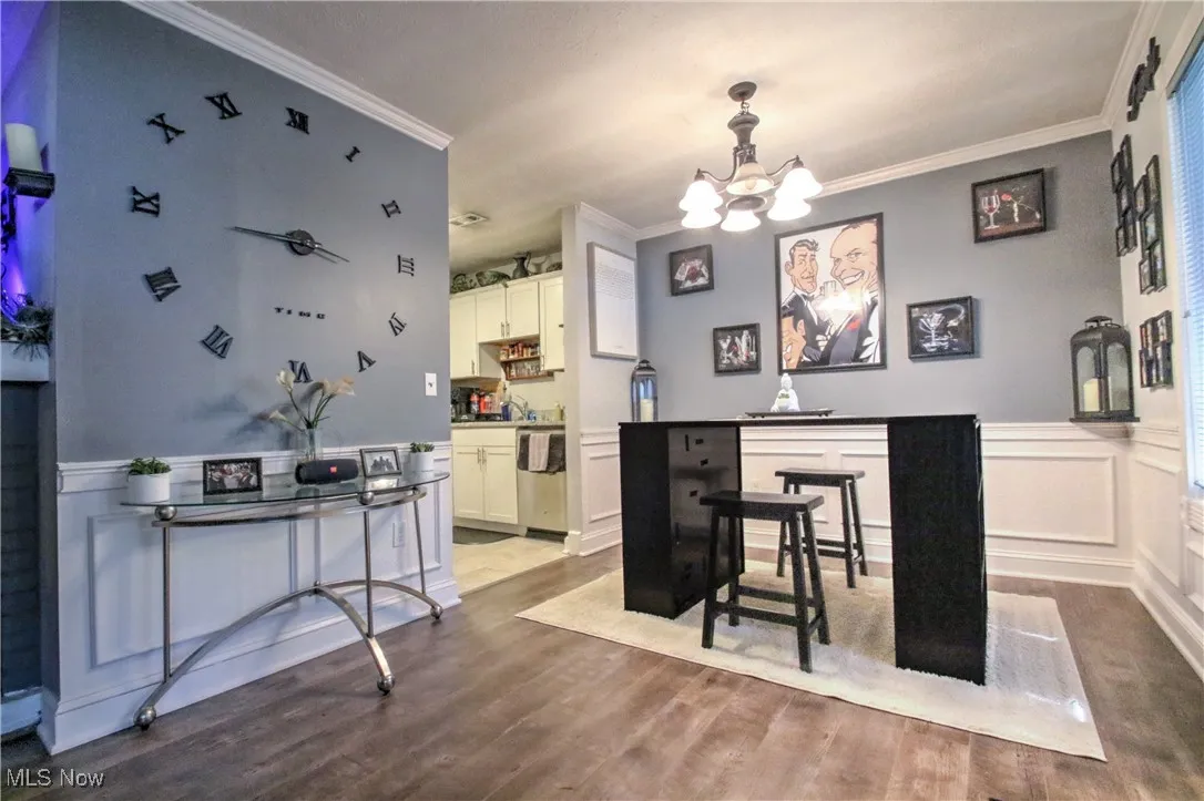Dining area with a wainscoted wall, a decorative wall, crown molding, wood finished floors, and a chandelier