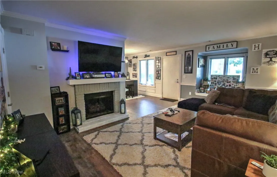 Living room with crown molding, wood finished floors, and a brick fireplace