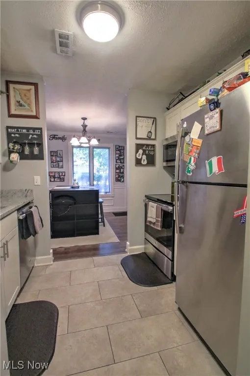 Kitchen featuring stainless steel appliances, white cabinetry, a textured ceiling, and light tile patterned floors