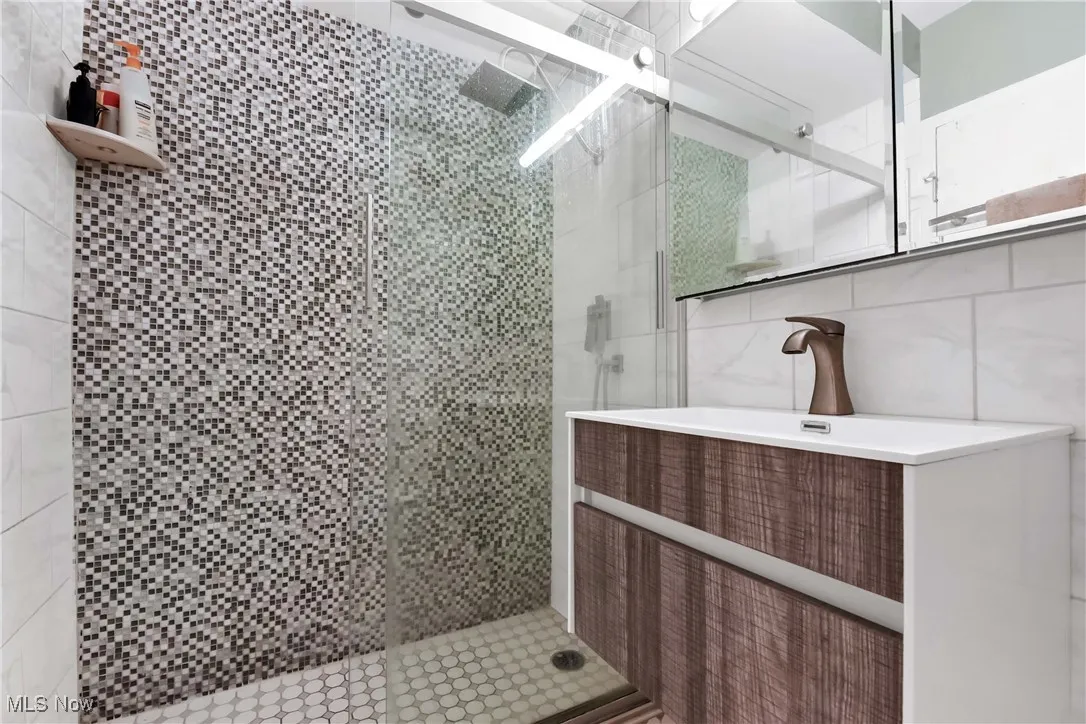 Bathroom with tile walls, a shower stall, and vanity