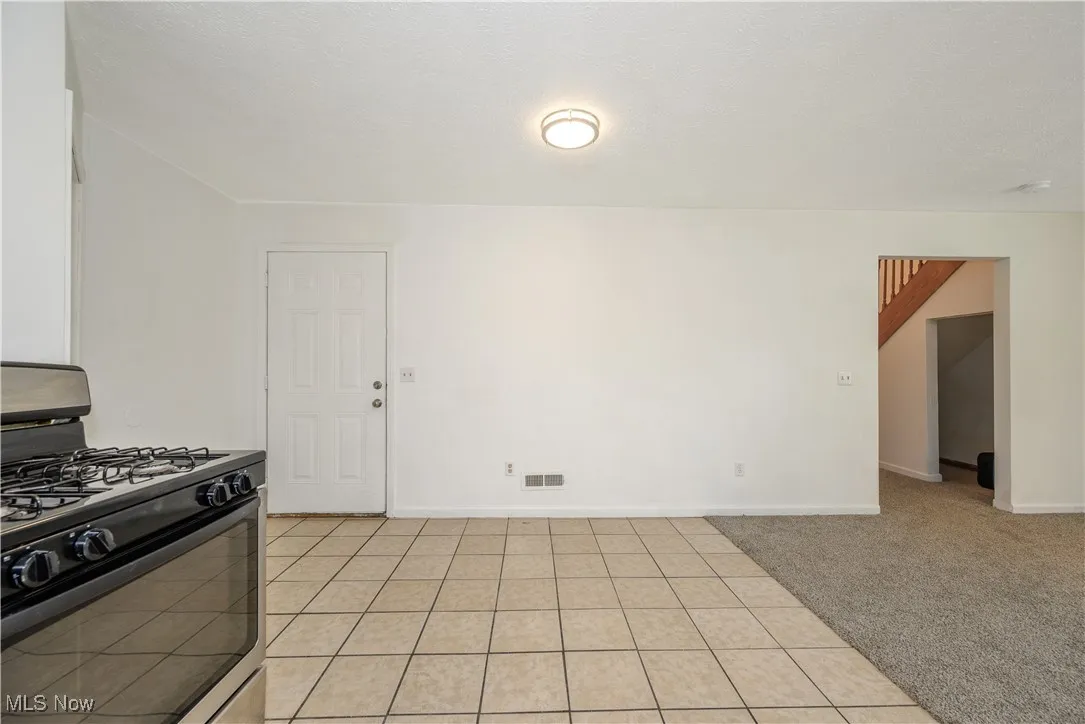 Kitchen with black range with gas cooktop, light tile patterned floors, light colored carpet, and a textured ceiling