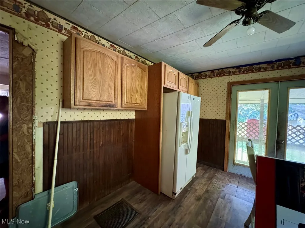 Kitchen with wallpapered walls, wainscoting, white refrigerator with ice dispenser, dark wood finished floors, and a ceiling fan