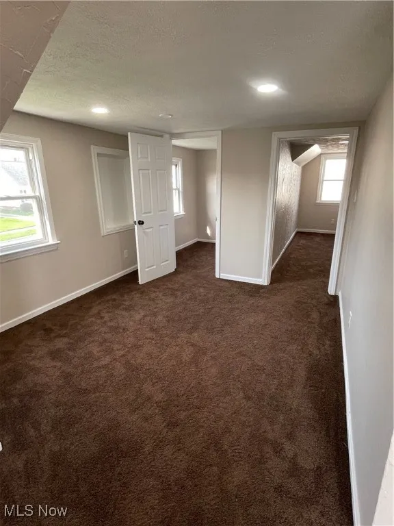 Below grade area featuring plenty of natural light, a textured ceiling, and dark colored carpet