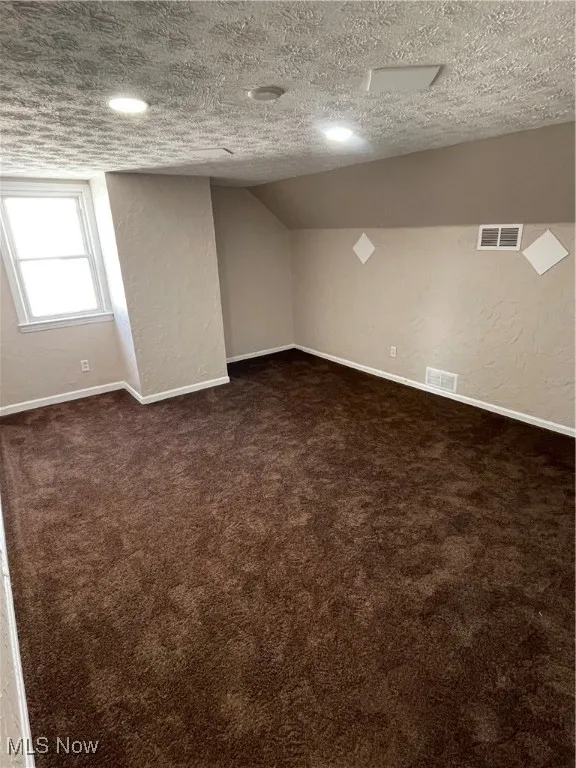 Below grade area with a textured wall, a textured ceiling, and dark colored carpet