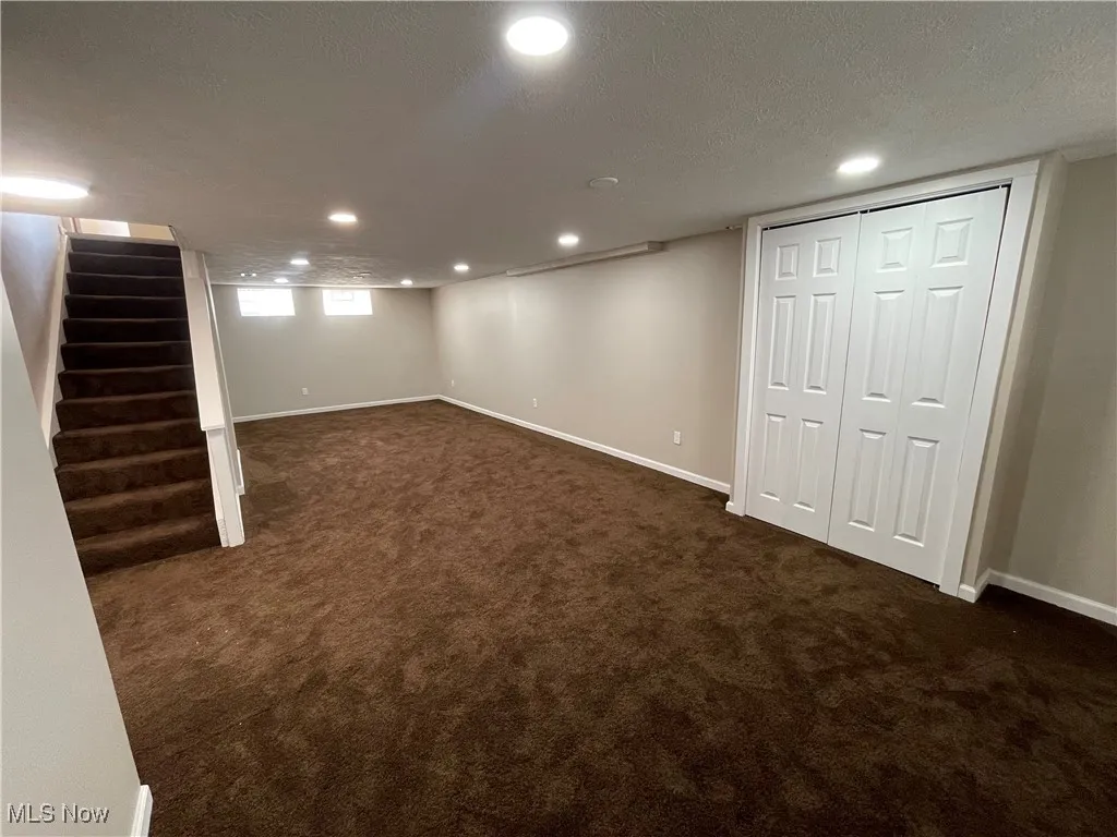 Below grade area with a textured ceiling, dark colored carpet, recessed lighting, and stairway