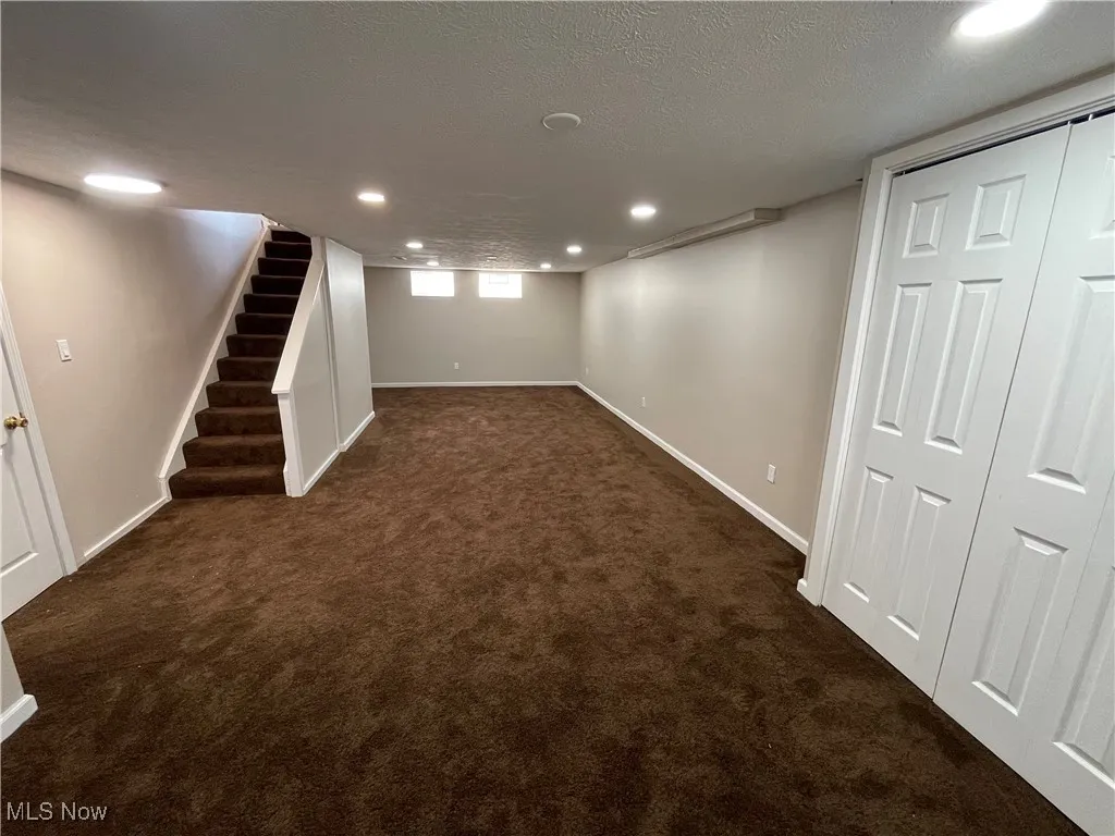 Basement with recessed lighting, dark colored carpet, a textured ceiling, and stairs